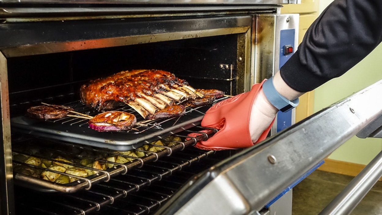 A oven mitt covered hand reaching into an oven to pull out a rack of ribs.