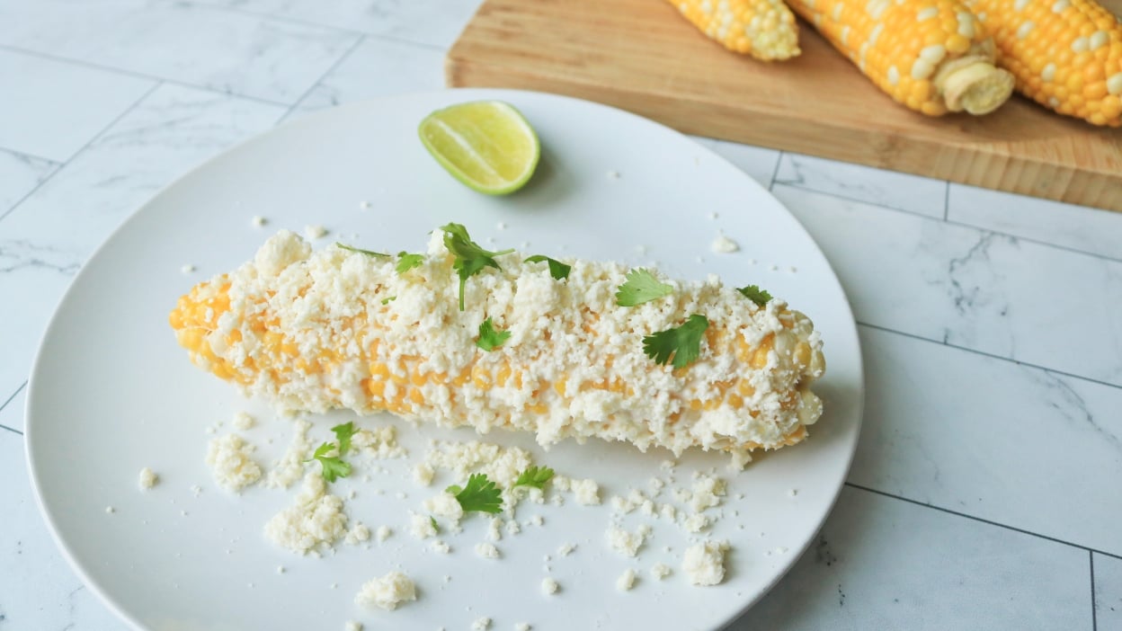 Elote on a plate in front of a cutting board of corn on the cob.