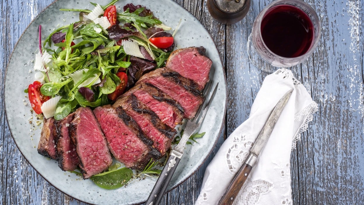 A sliced steak next to salad on a plate.