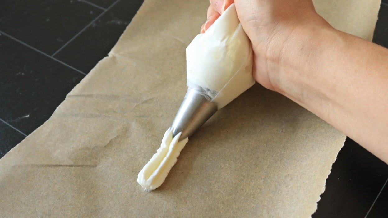 A hand piping white frosting.