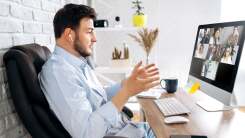 A man sitting in front of a computer speaking on a video call with his hands in the air