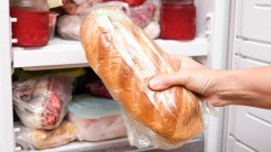 Hand putting a loaf of wrapped bread in the freezer.