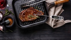 A steak on a grill pan with a meat thermometer sticking out.