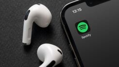 The Spotify app logo on an iPhone with AirPods lying nearby