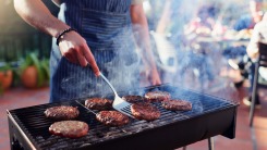 A person grilling hamburgers on a charcoal grill.