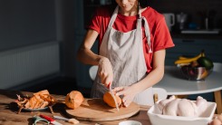 A woman wearing an apron and chopping squash.