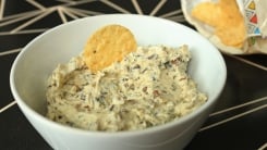 A bowl of dip with a.round tortilla chip in it.