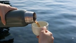 Person's hand pouring wine out of a thermos and into a mug.