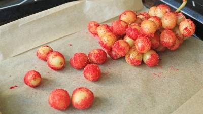 Grapes covered in red Jell-O powder on a baking sheet.