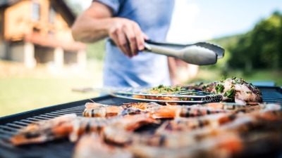 A man's hand with tongs over a grill outside.