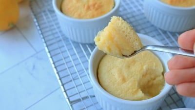 A hand holding a spoonful of lemon pudding cake in front of the other small cakes.