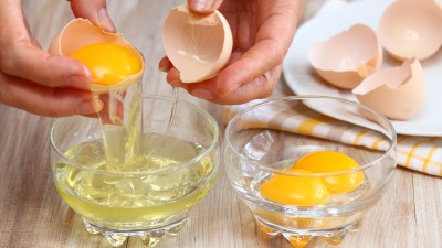 Hands separating egg whites and yolks into two bowls.