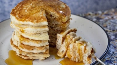 A tall stack of pancakes with a big bite cut out.