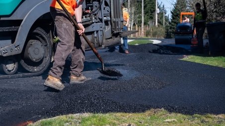 Construction worker shoveling freshly laid asphalt 