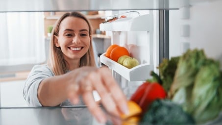 A woman organizes vegetables in the fridge.