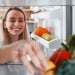 A woman organizes vegetables in the fridge.