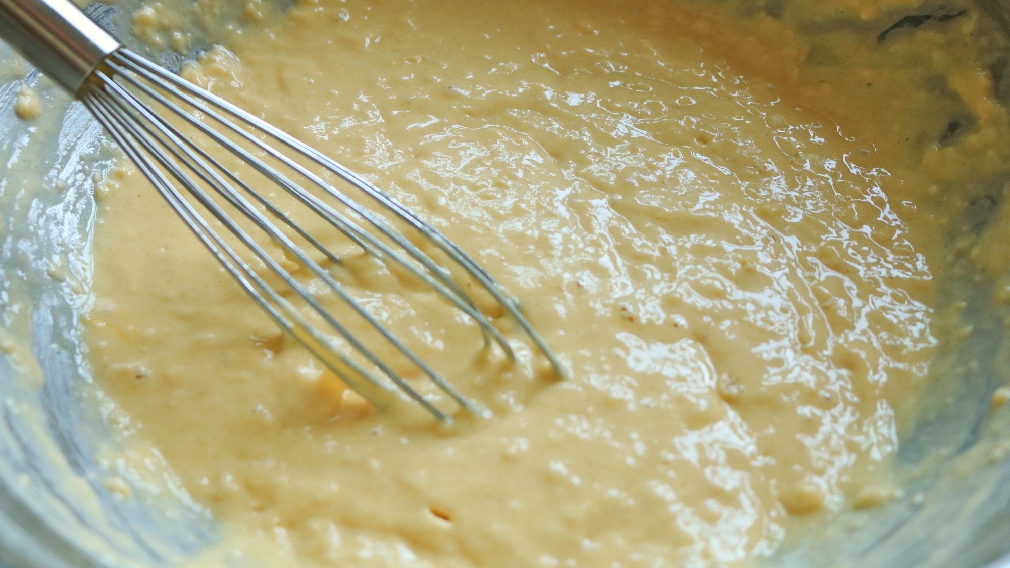 Lumpy pancake batter in a bowl with a whisk.