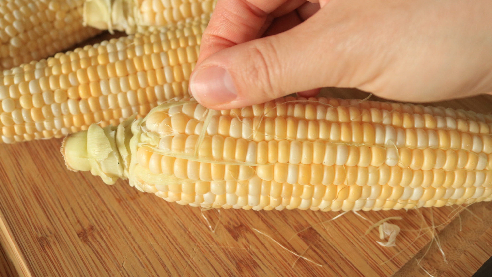 Hand peeling the silk off an ear of corn.