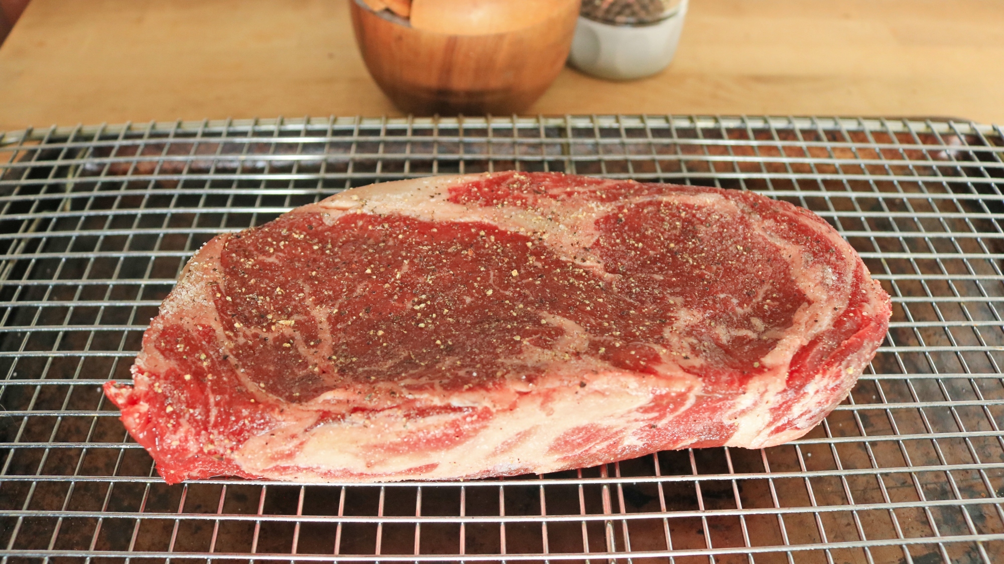 A raw steak on a wire rack over a baking sheet pan.