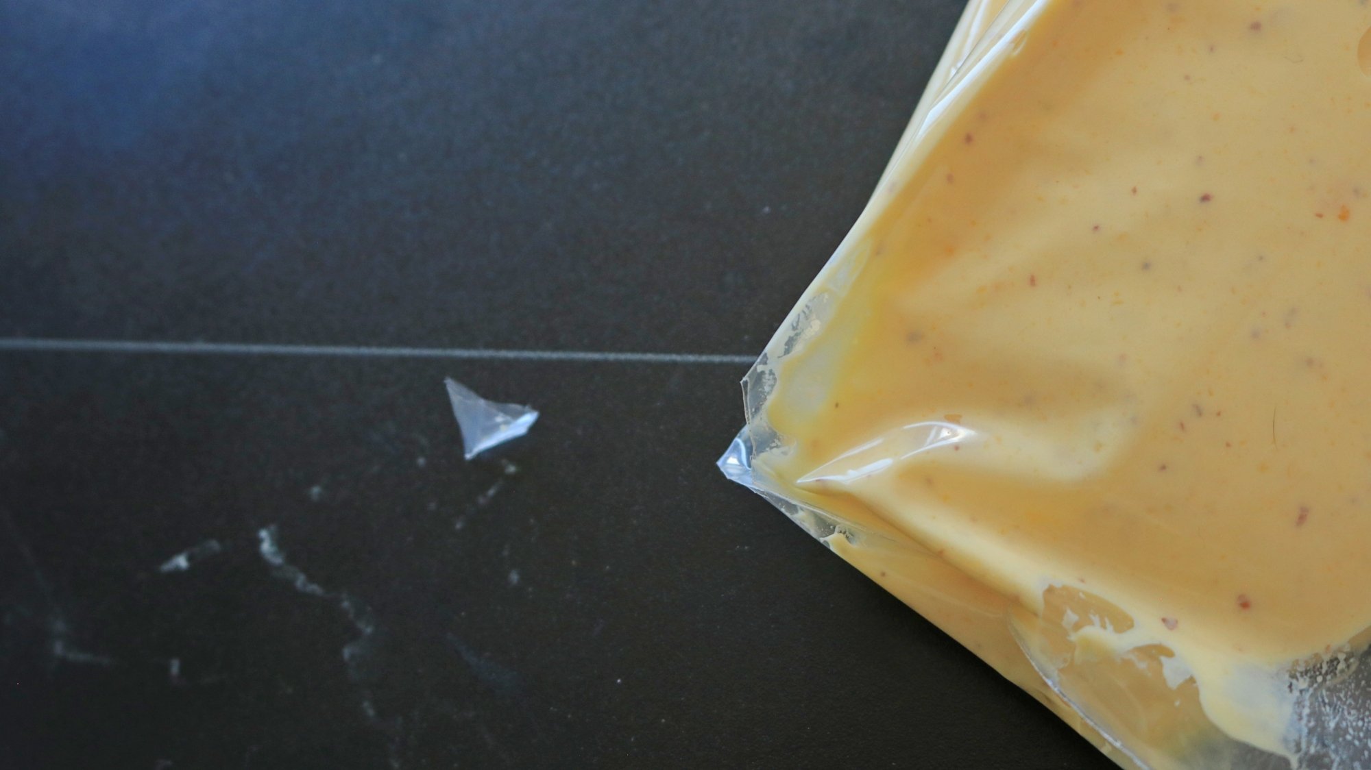 A close up of a plastic bag filled with yellow filling and the corner is snipped.