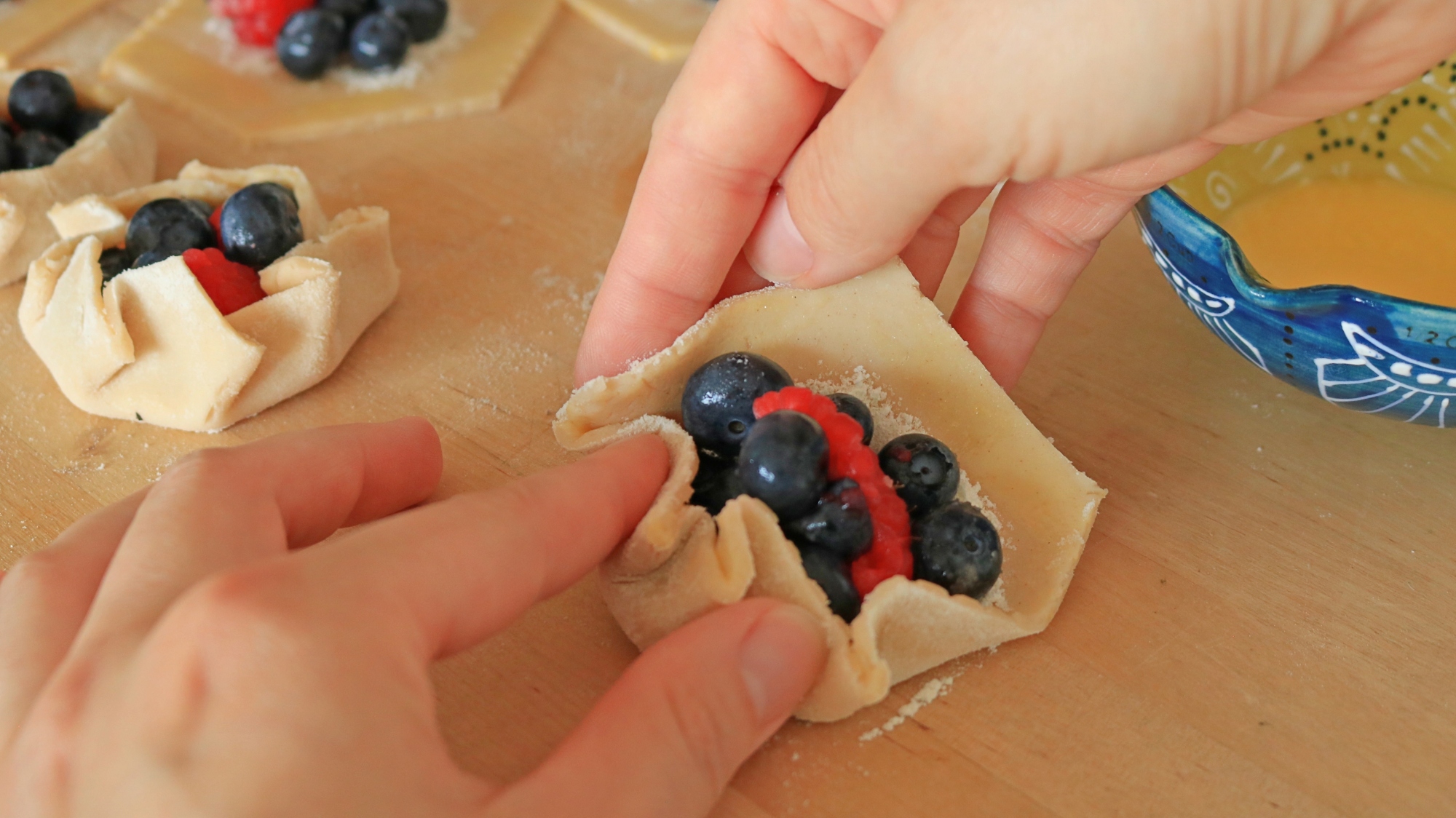 Hands pleating the crust on fruit galettes.