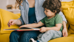 A woman and a young child sitting together on a couch, reading a book