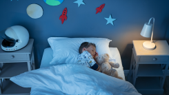 A young kid sleeping in a twin bed with a teddy bear. Rocket ships and other space-themed decorations on the wall.